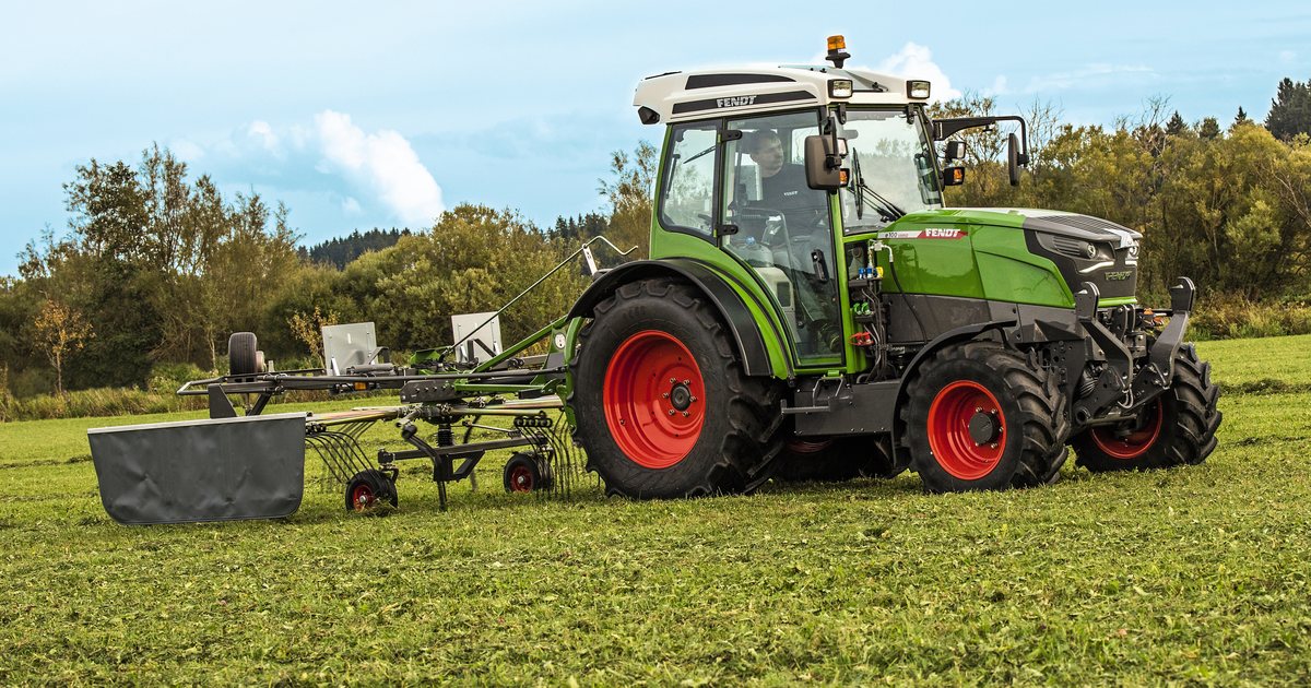 Trator elétrico Fendt e100 Vario puxando enleirador em campo de feno