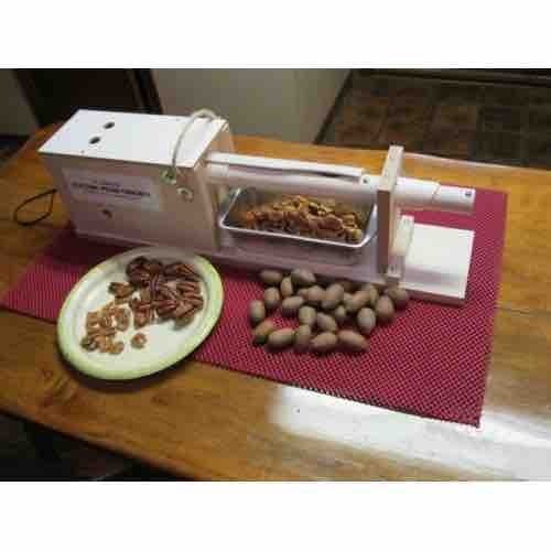 Quebrador elétrico de noz pecan Kinetic Kracker sobre uma mesa, com nozes inteiras e amêndoas quebradas